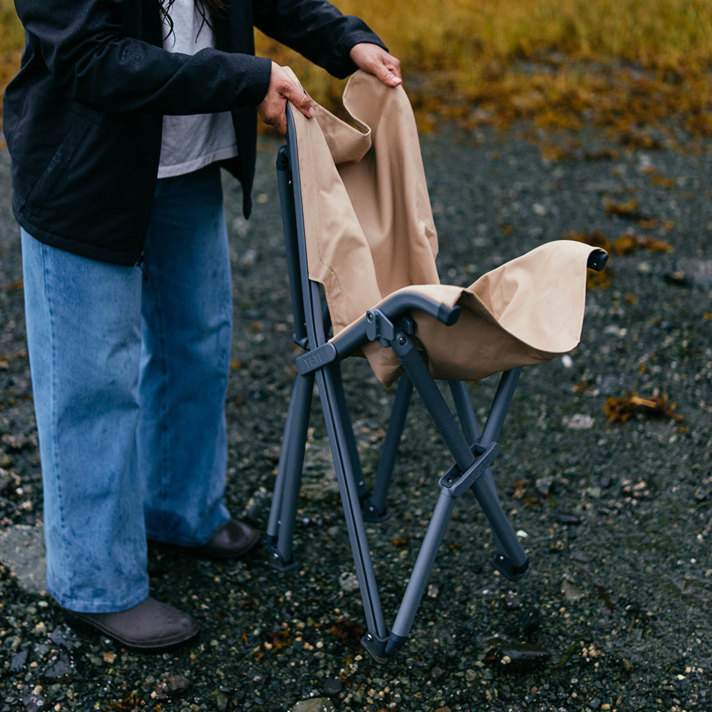 Person holding a beige jacket over a folding YETI field chair outdoors