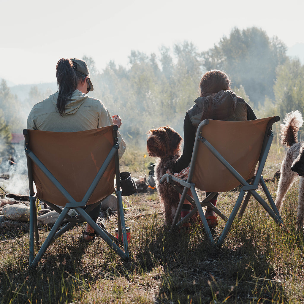 Two people sitting in YETI Field chairs with a dog in a field