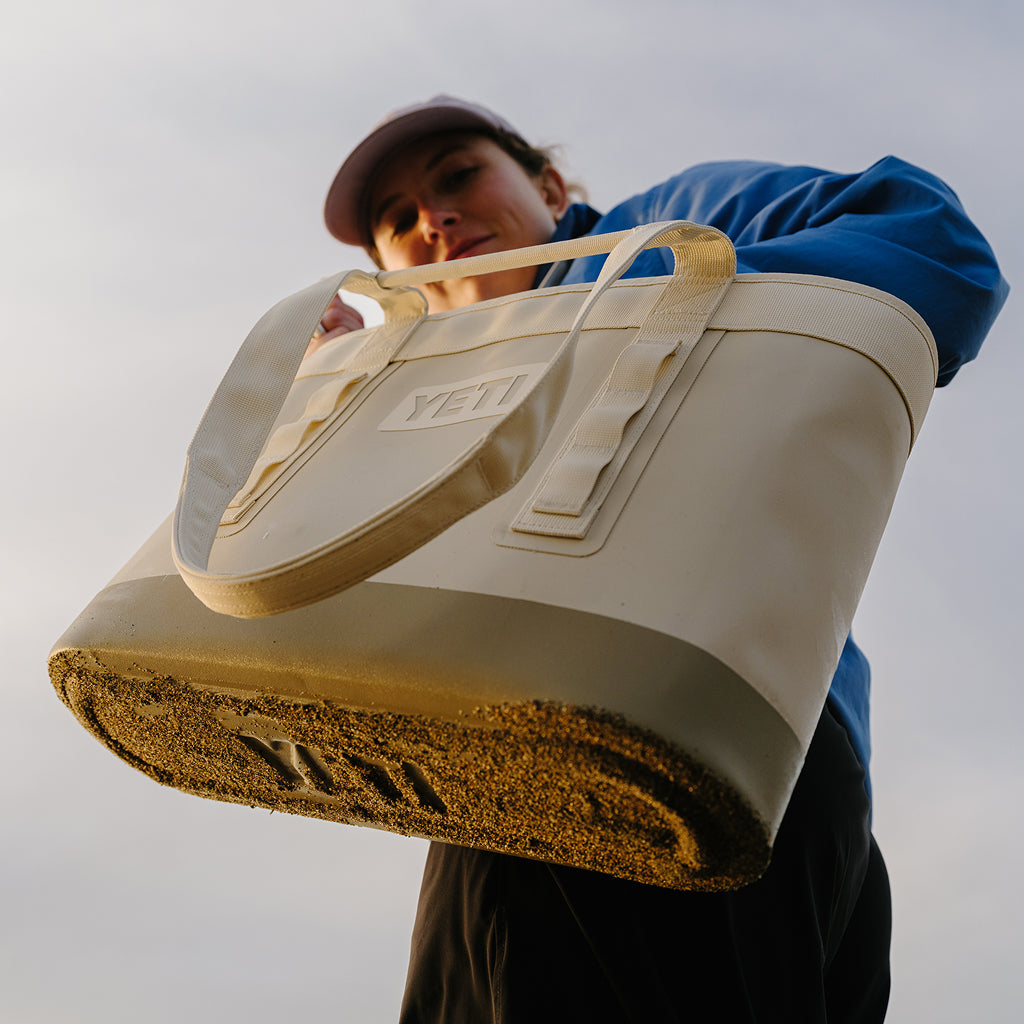 Person holding a beige YETI bag against a plain background
