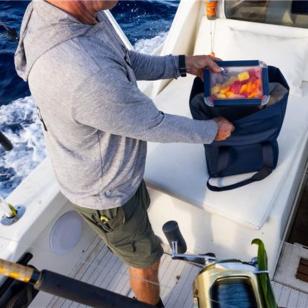 Man on a boat, opening his YETI soft cooler with a lunch box of fruit in it.