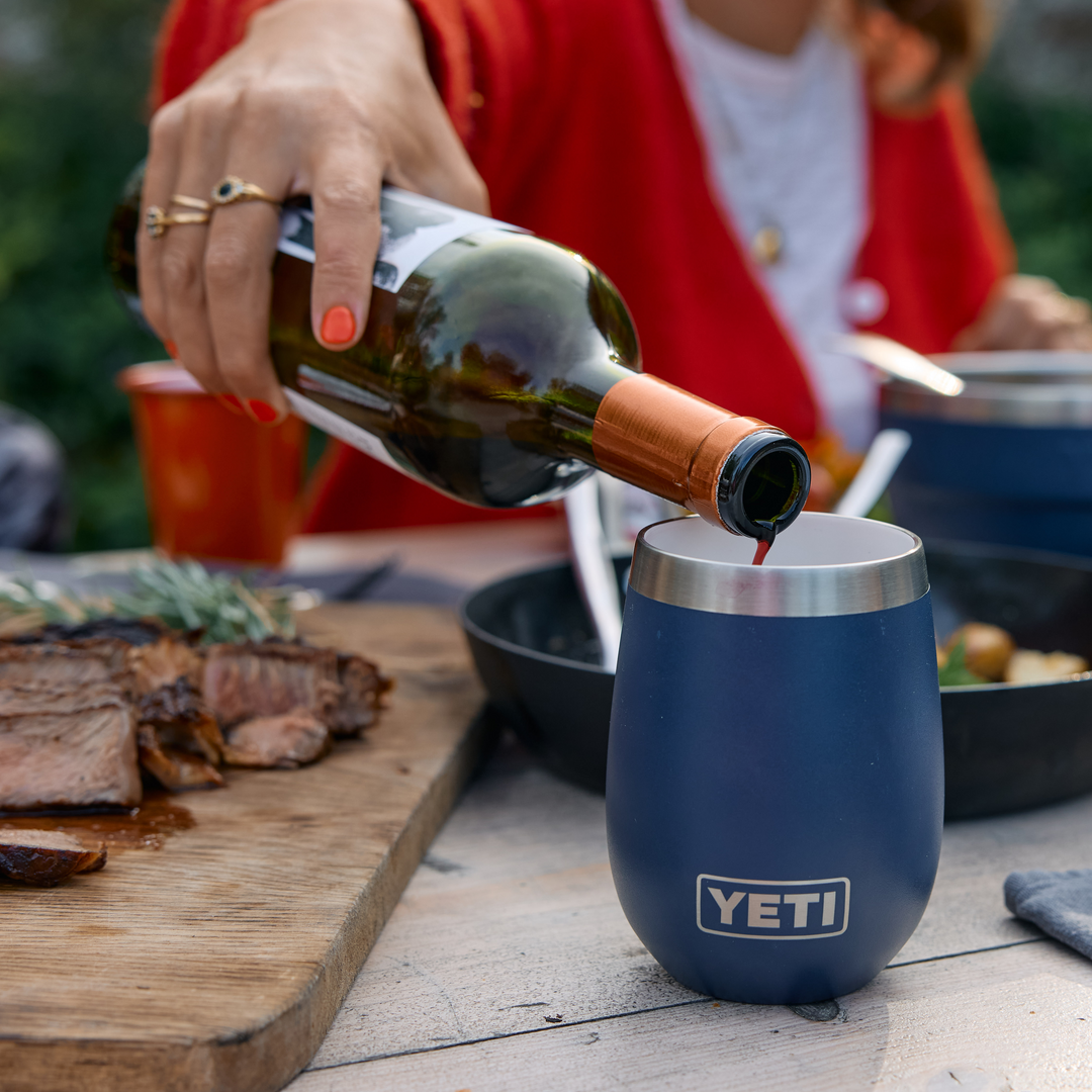 Person pouring wine into a blue YETI wine tumbler at an outdoor meal.
