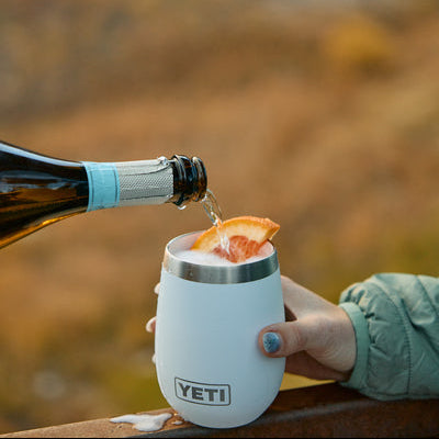Person pouring a drink from a bottle into a YETI-branded wine tumbler outdoors.